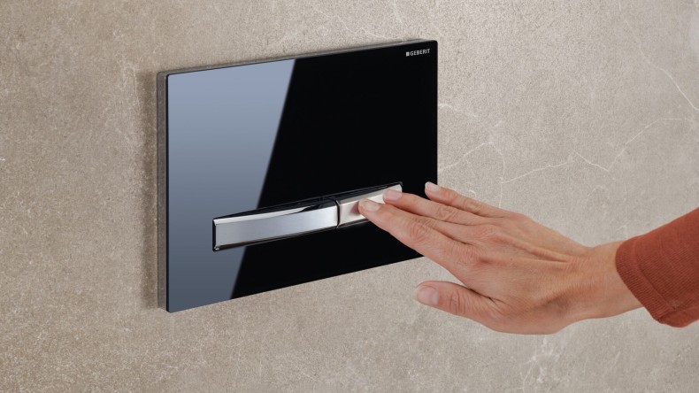 A hand activates the flush on a black Sigma50 actuator plate (© Geberit)