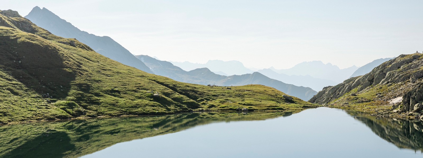 Bergsee in grüner Landschaft mit Bergketten im Hintergrund (© Geberit)