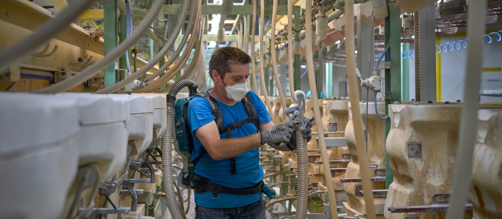 A man, wearing a mouth guard and equipped with a backpack hoover, is vacuuming hoses that lead to plaster moulds. A man, wearing a mouth guard and equipped with a backpack hoover, is vacuuming hoses that lead to plaster moulds.