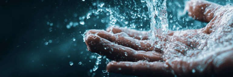 A human hand catching water as it pours down and splashes from above.