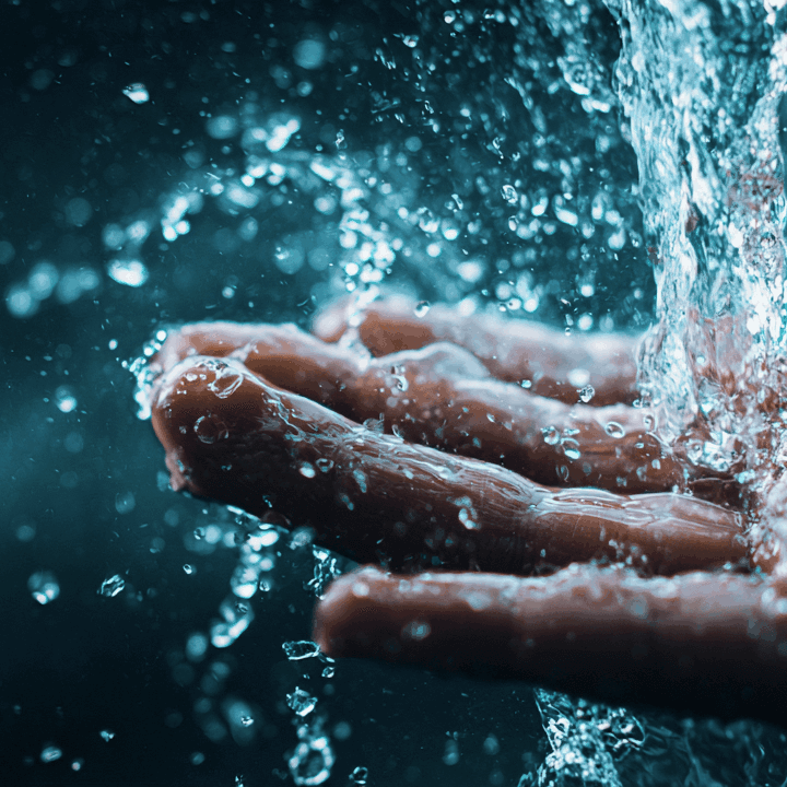 A human hand catching water as it pours down and splashes from above.