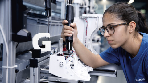 Eine junge Frau in Brille und blauem T-Shirt ist in der Fabrik und arbeitet an der elektrischen Ausstattung eines Dusch-WCs.