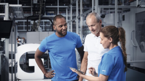 Drei Techniker, die sich in einem Hightech-Produktionswerk befinden und in ein Tablet schauen.