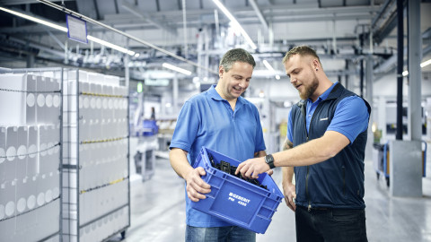 Two men inspect a blue storage container in a warehouse setting.