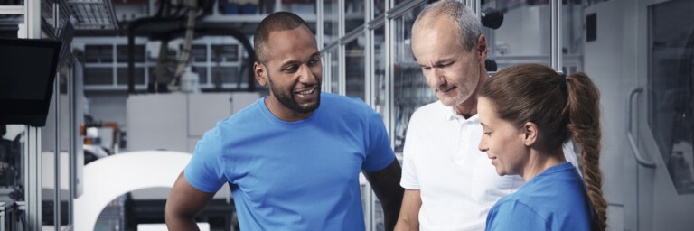 Drei Techniker, die sich in einem Hightech-Produktionswerk befinden und in ein Tablet schauen.