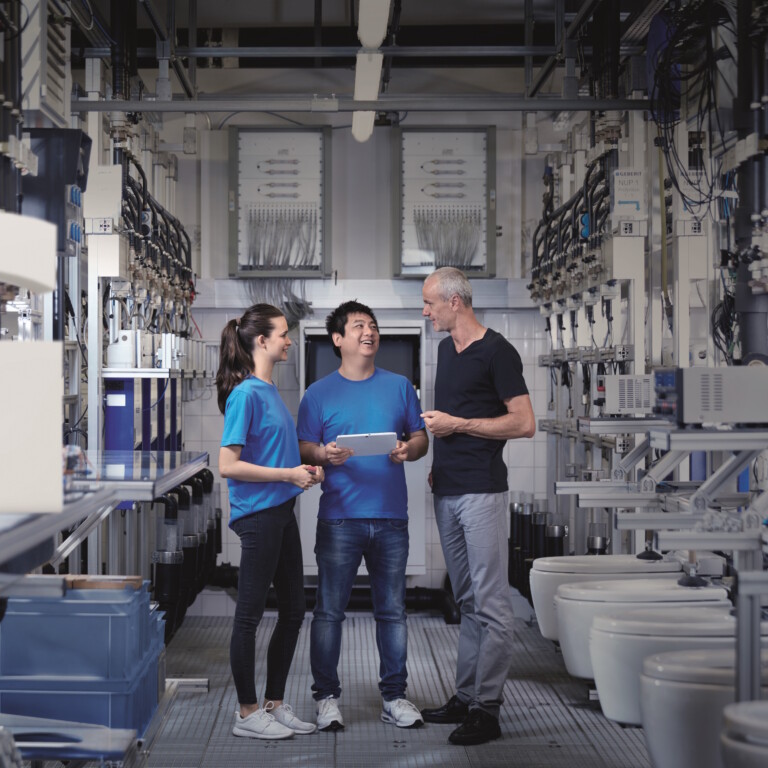 Three technicians are in a sanitary testing facility. A white letter ‘G’ is placed in the left-hand section of the image.