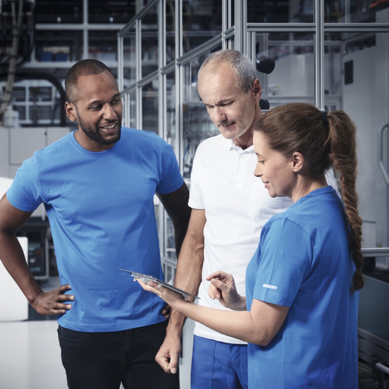 Drei Techniker, die sich in einem Hightech-Produktionswerk befinden und in ein Tablet schauen.
