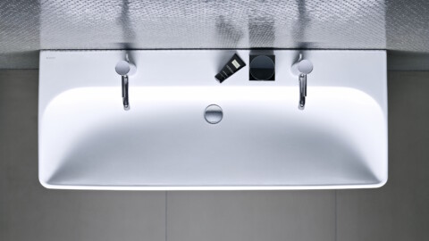 Von oben gesehenes weisses, rechteckiges Waschbecken mit zwei Wasserhähnen und Pflegeprodukten.