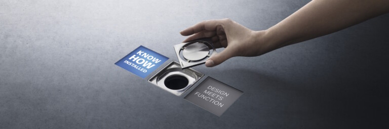 A hand places a drain cover over a square floor drain between the two claims ‘Know-how Installed’ and ‘Design Meets Function’.