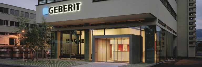 Modern multi-storey Geberit headquarters with illuminated logo at dusk