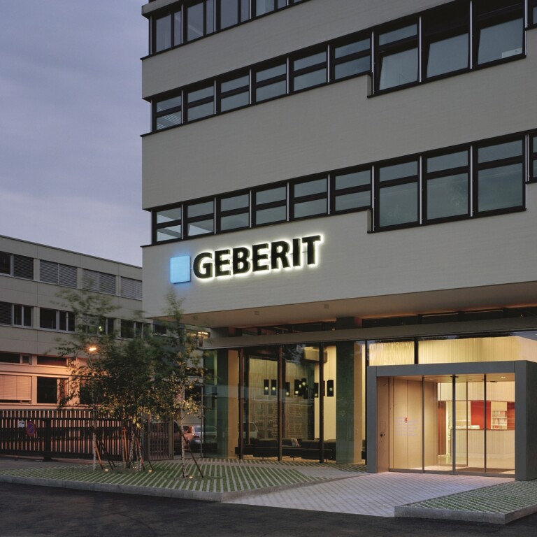 Modern multi-storey Geberit headquarters with illuminated logo at dusk