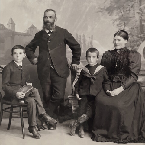 A family photograph of the founding Gebert family, with mother, father and two sons dressed elegantly in front of an ornate background.