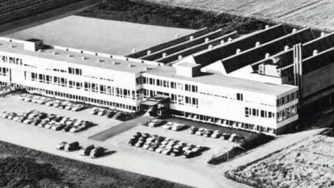 Luftaufnahme eines modernen, grossen Gebäudes mit einem angrenzenden Parkplatz, voll mit geparkten Autos.