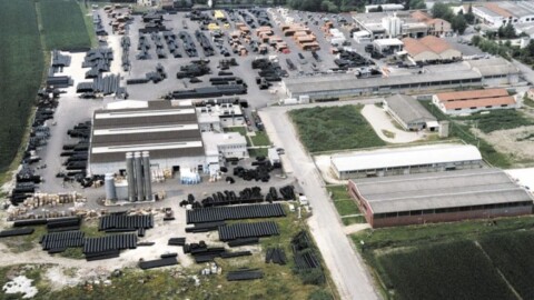 Luftaufnahme einer weitläufigen Fabrikanlage mit mehreren Hallen und grossen Lagermengen schwarzer Rohre im Freien