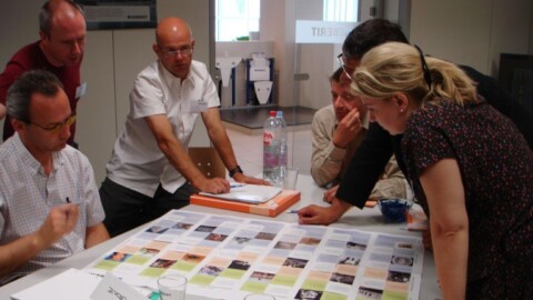 Eine Gruppe von sechs Personen beugt sich über eine grosse, bedruckte Karte, die auf einem Tisch liegt.