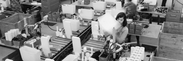 Industriehalle mit Förderbändern, an denen Mitarbeitende in einer Fabrik Spülkästen bearbeiten.