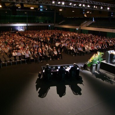 A large, dark auditorium filled with people looking towards a stage.