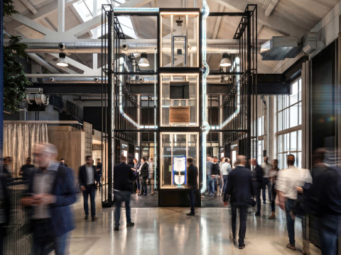 A busy indoor exhibition space featuring a large, modern display structure surrounded by people.