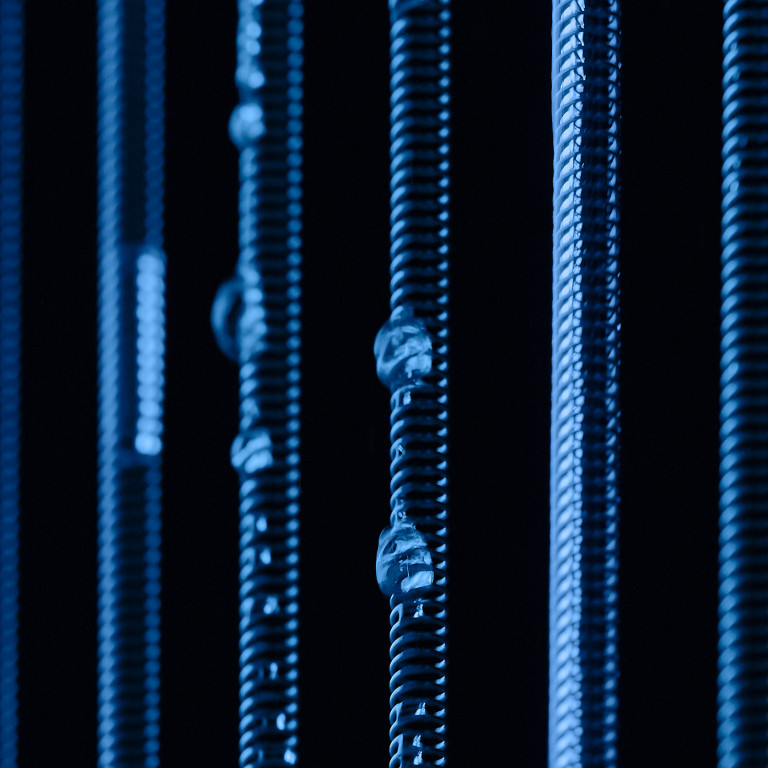 Vertical springs with varying widths and small droplets, illuminated in blue against a dark background.