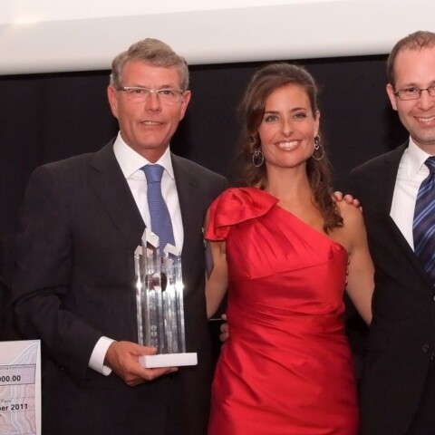 A group of five individuals posing together at an award ceremony, with one holding a trophy and another holding a large check.