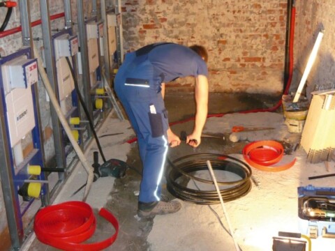 Ein Handwerker in blauer Arbeitskleidung organisert Kabelrollen in einem unvollendeten Raum mit freiliegenden Ziegelwänden.