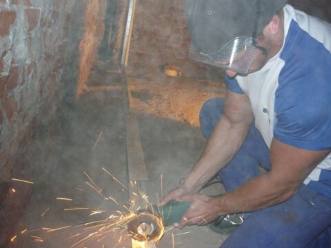 Ein Mann mit Schutzbrille und Maske schneidet mit einer Trennscheibe Metall, Funken fliegen in einem dunklen Raum.