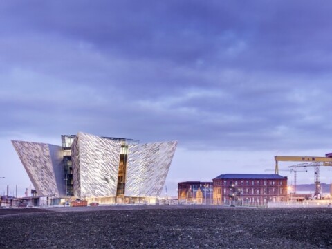 Die Titanic-Attraktion mit einer modernen Fassade und einem Industriegelände im Hintergrund unter einem bewölkten Himmel.