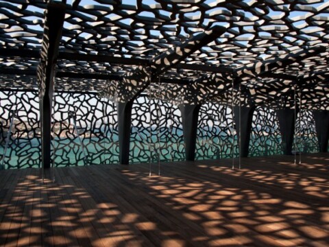 An interior space with a patterned ceiling casting intricate shadows on the wooden floor.