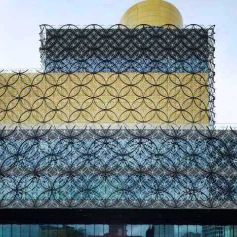 Eine moderne, mehrschichtige Architektur und geometrischen Mustern an der Fassade, vor bewölktem Himmel.