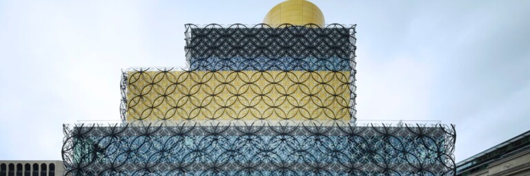 Eine moderne, mehrschichtige Architektur und geometrischen Mustern an der Fassade, vor bewölktem Himmel.