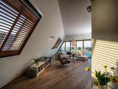 Modernes Wohnzimmer mit schrägen Fenstern, Holzfussboden und hellen Akzenten.