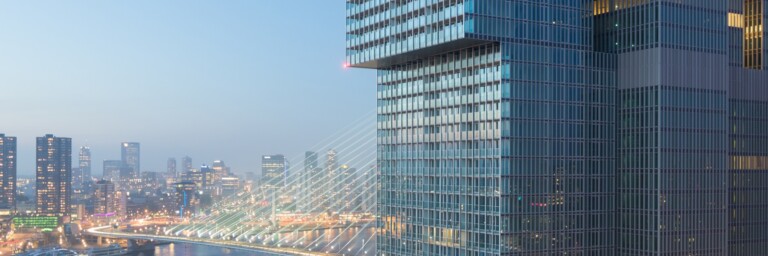Moderne Wolkenkratzer mit Glasfassade und Blick auf eine Stadtbrücke bei Abenddämmerung.