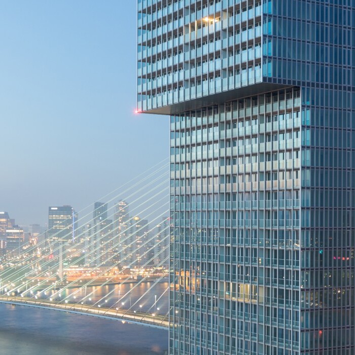 Moderne Wolkenkratzer mit Glasfassade und Blick auf eine Stadtbrücke bei Abenddämmerung.