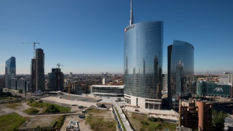 Moderne Wolkenkratzer in einer urbanen Umgebung, mit einem blauen Himmel und Baustellen im Hintergrund.