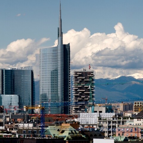 City skyline featuring modern skyscrapers and mountains in the background under a partly cloudy sky.