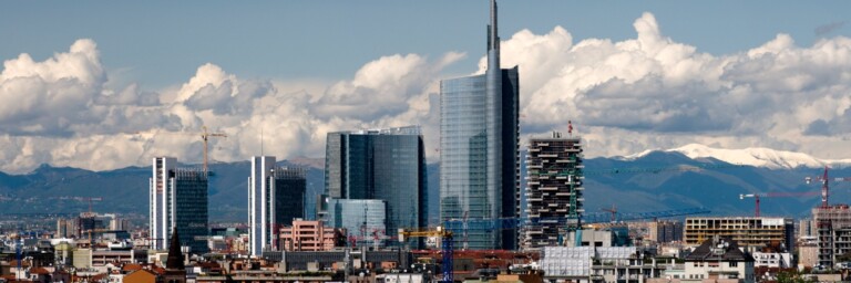 Skyline einer Stadt mit modernen Wolkenkratzern und Bergen im Hintergrund unter einem bewölkten Himmel.