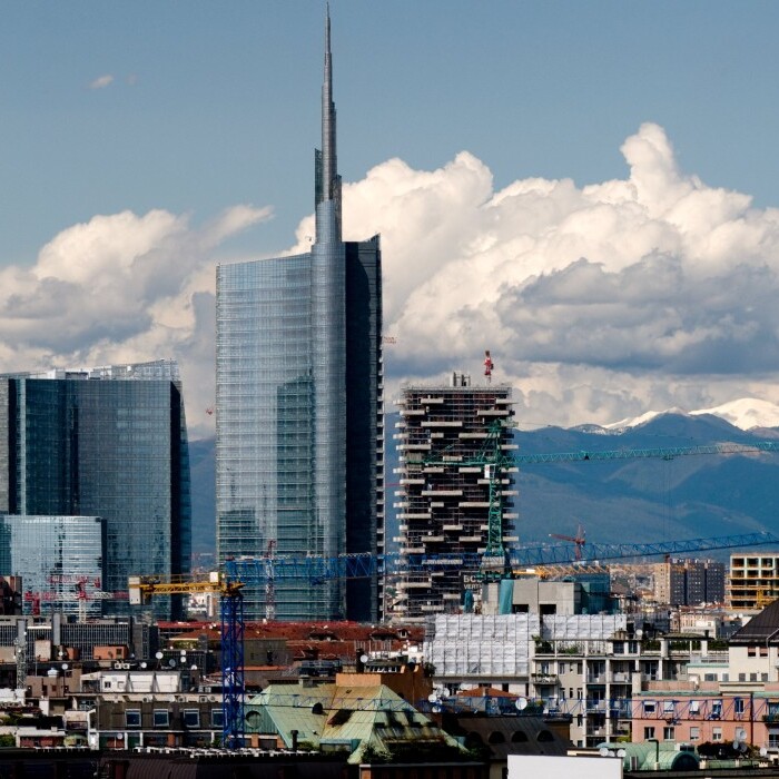 Skyline einer Stadt mit modernen Wolkenkratzern und Bergen im Hintergrund unter einem bewölkten Himmel.