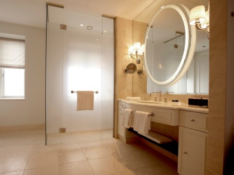 A modern bathroom featuring a glass shower, elegant round mirror with backlighting, and a white vanity with neatly arranged towels.