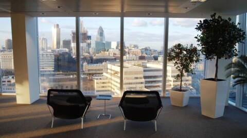 A modern office space with two black chairs and a small table, showcasing a city skyline through large windows.