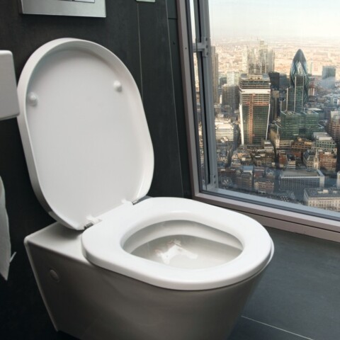 A modern bathroom featuring a toilet with an open lid,  and a large window showcasing a cityscape view.