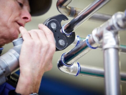 Ein Handwerker verwendet ein Mapress Verpressungswerkzeug, um Metallrohre zusammenzufügen.