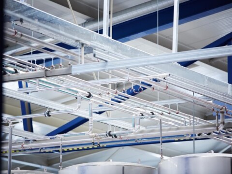 Ein Innenraum mit einem industriellen Dach, das von Metallträgern und Rohren durchzogen ist.