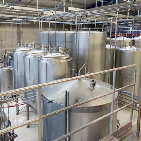 Eine industrielle Brauerei mit grossen silbernen Lagertanks und einem kupfernen Sudkessel.