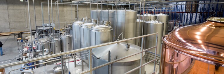 Eine industrielle Brauerei mit grossen silbernen Lagertanks und einem kupfernen Sudkessel.