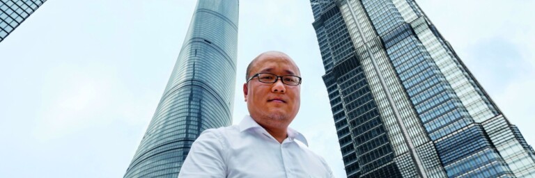 Eine Person steht im Vordergrund zwischen zwei hohen Wolkenkratzern unter einem bewölkten Himmel.