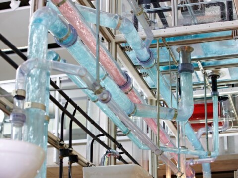 A complex water tower with transparent pipes and colored water flowing through them, set within a modern industrial environment.
