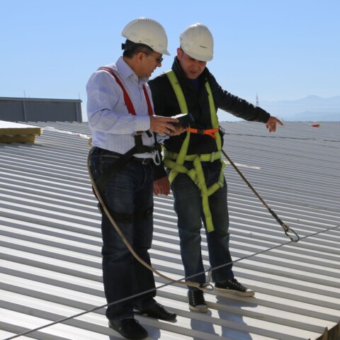 Two construction workers in safety gear inspect a rooftop.
