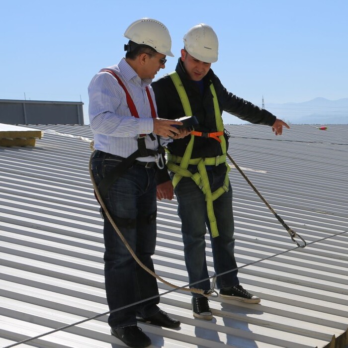 Two construction workers in safety gear inspect a rooftop.