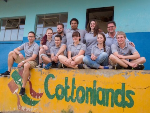 Eine Gruppe von zehn Personen in grauen T-Shirts sitzt auf einer bunten Mauer mit der Aufschrift "Cottonlands".