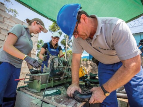 Eine Gruppe von drei Personen arbeitet an einer Maschine unter einem grünen Pavillon.